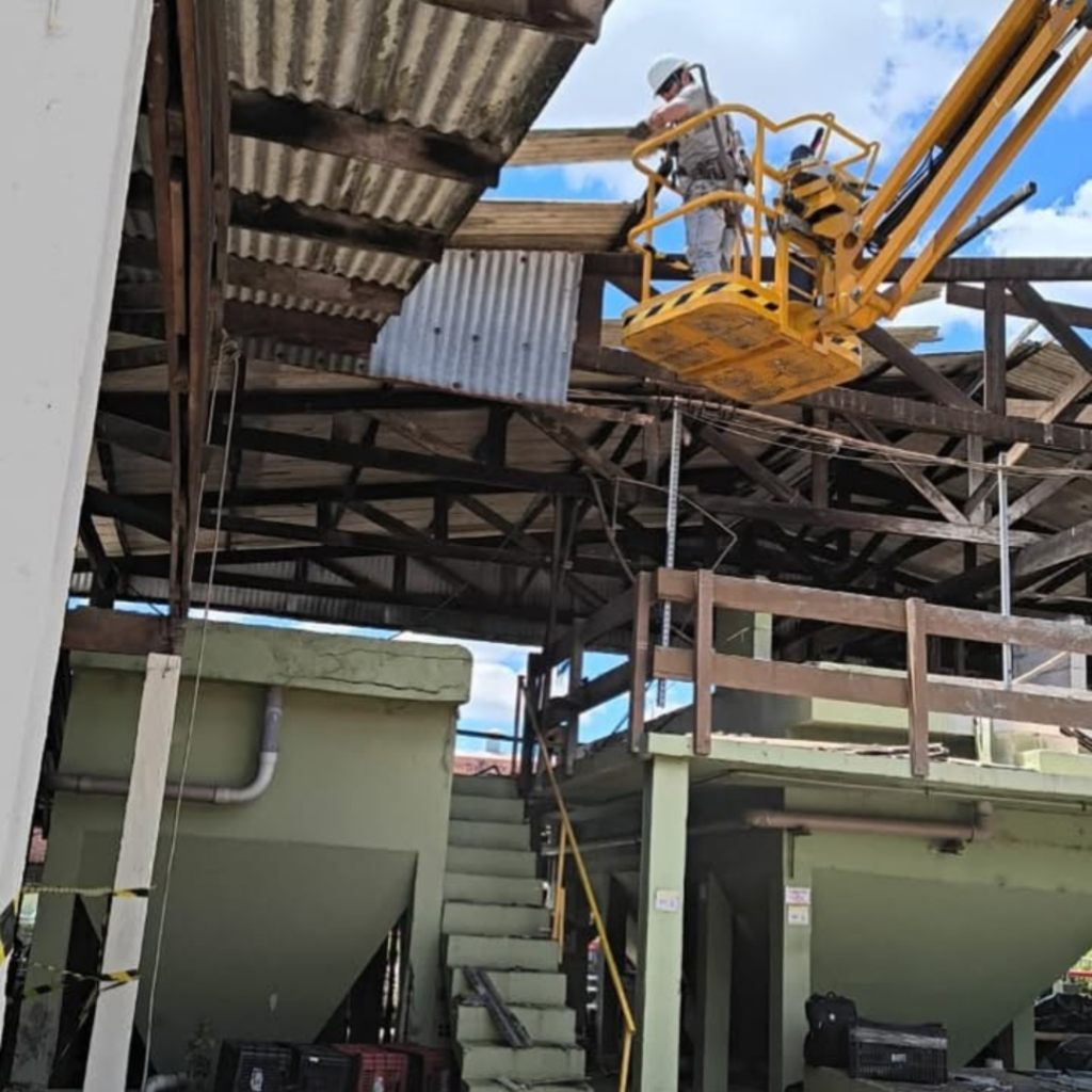 Equipe de engenharia realizando reforma e manutenção de telhado industrial utilizando plataforma elevatória.